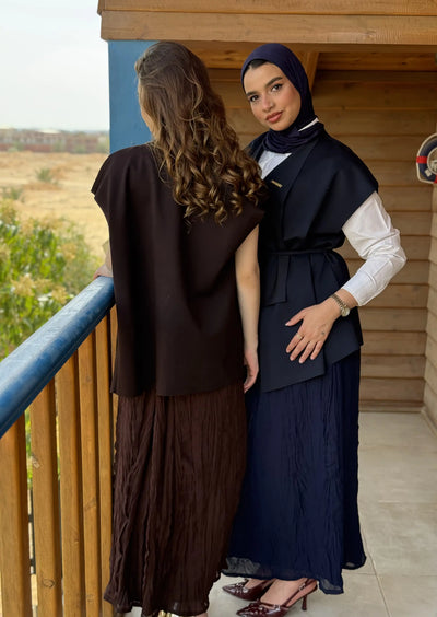 Two women standing on a balcony with one wearing a hijab and a dark outfit.