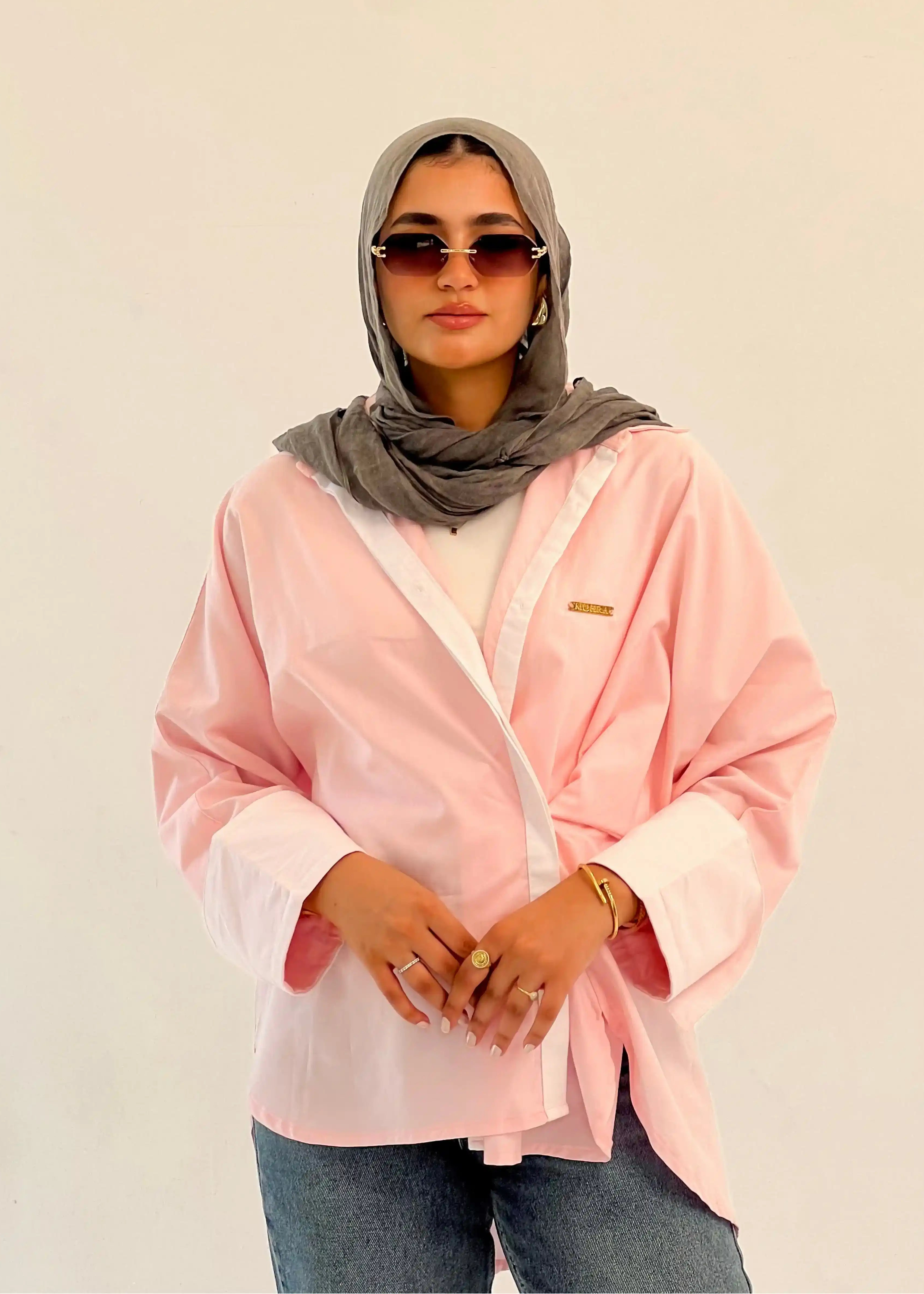 Person wearing a pink shirt, gray hijab, and sunglasses against a beige background Main image
